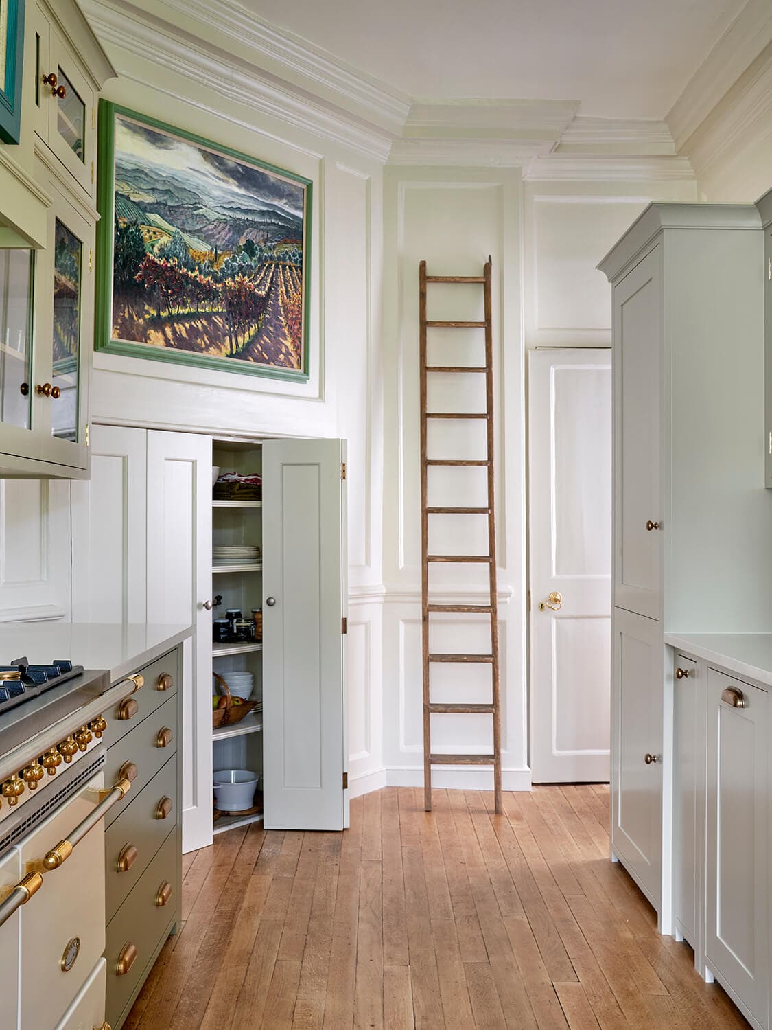 Tall kitchen cabinetry reached by a library ladder on a brass rail