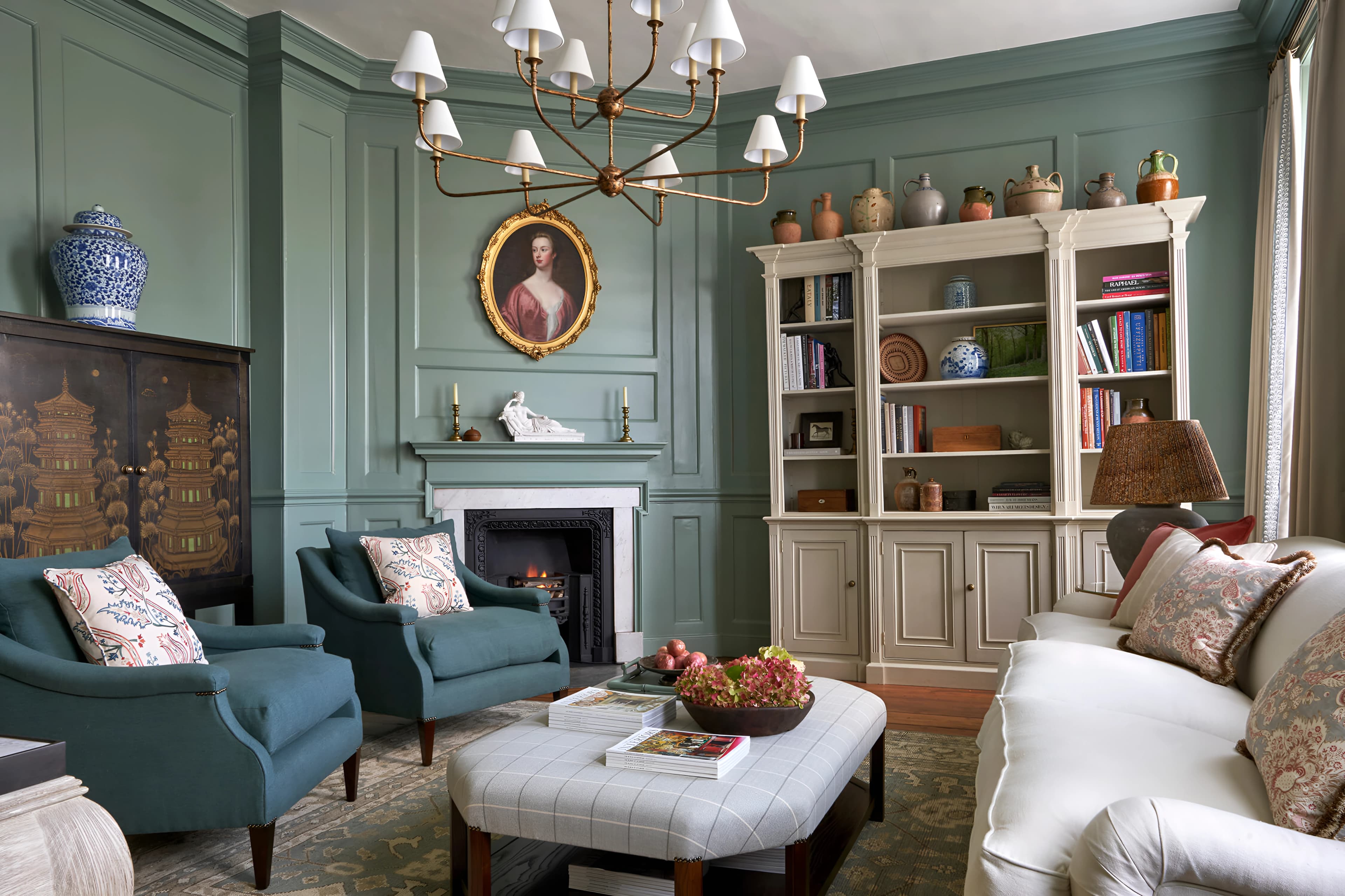The drawing room's original marble fireplace, framed by soft green panelling, a portrait above the mantel and bespoke bookcases alongside