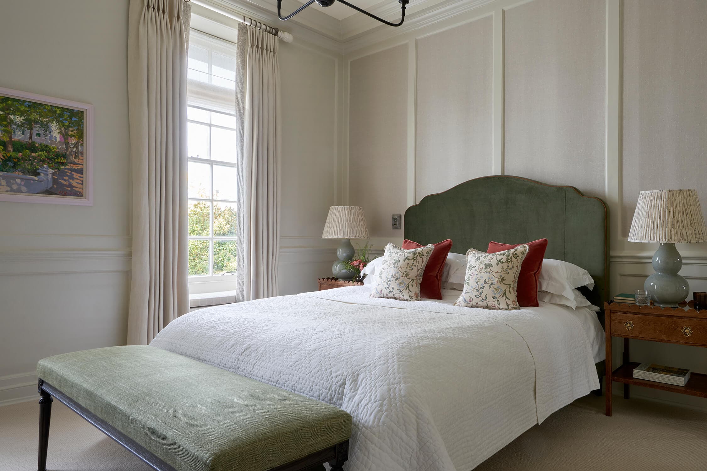 The principal bed with a green velvet headboard, layered white bedding and pleated bedside lamps either side